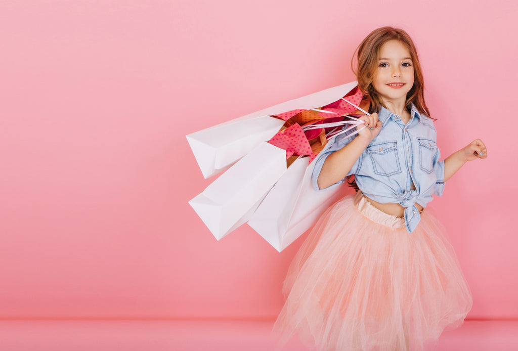 little girl with shopping bags in front of pink background