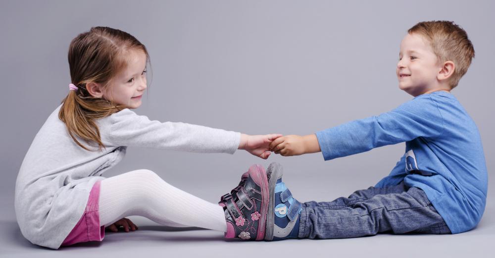 a little girl and a boy sitting on the ground playing and smiling, looking happy in their new shoes.