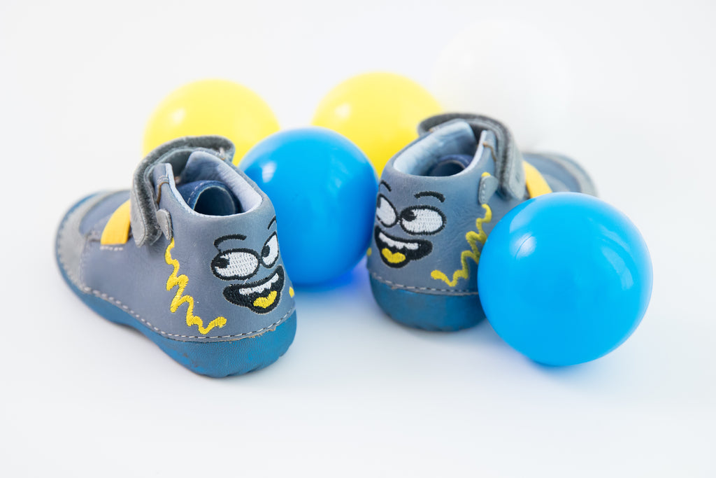 picture of a pair of first walker boots and a couple of blue and yellow balls. the boots have a funny face decorated on the heels